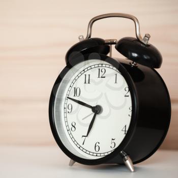 Black alarm clock is on a white bedside table near wooden wall