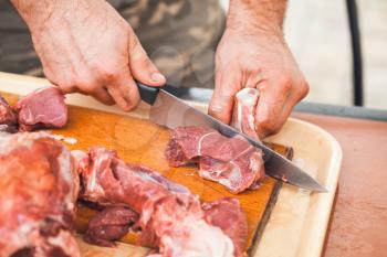 Lamb meat cutting, strong cook hands with knife. Close-up photo, selective focus