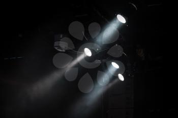 Group of spot lights with strong beams in smoke over dark background, modern stage illumination equipment