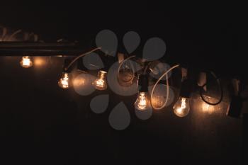Old style garland of vintage tungsten bulb lamps hanging on dark wall at night. Close up photo with selective focus