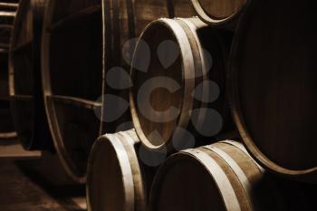 Wine storage. Round wooden barrels in dark winery, close-up photo with selective focus