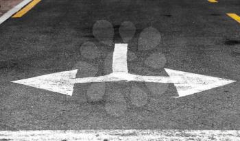 Only turns left or right. White double arrow, road marking over black highway asphalt. Close-up photo with selective focus