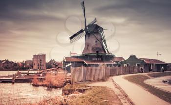 Old wooden windmill on Zaan river coast, Zaanse Schans town, popular tourist attractions of the Netherlands. Suburb of Amsterdam. Photo with gradient tonal correction filter effect