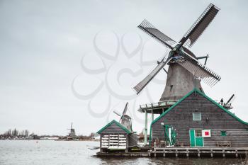 Old wooden windmills on Zaan river coast, Zaanse Schans town, popular tourist attractions of Netherlands. Suburb of Amsterdam
