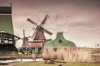 Old wooden barns and windmill on Zaan river coast. Zaanse Schans, popular tourist attractions of the Netherlands. Suburb of Amsterdam. Vintage tonal correction filter