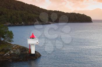 Lighthouse on the coast of Norwegian Sea. White tower red top stands on coastal rocks