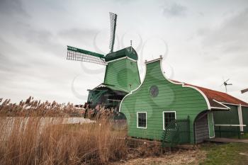 Windmill near green barn on Zaan river coast, Zaanse Schans town, popular tourist attractions of the Netherlands. Suburb of Amsterdam