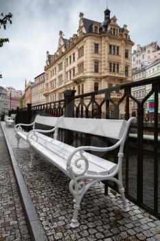 Empty street bench stands on Tepla river coast, street view of  Karlovy Vary town, Czech Republic