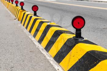 Concrete blocks with striped caution pattern, road fence with red reflectors