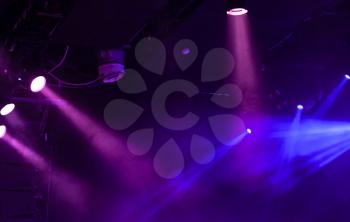Blue and purple scenic lights with strong beams in smoke over dark background, modern stage illumination equipment