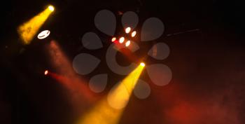 Red and yellow spot lights with strong beams in smoke over dark background, modern stage illumination equipment