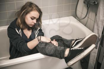 Stressed sad European teenage girl sitting in empty bath. Depression mood concept