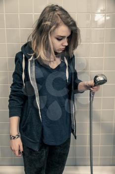 Stressed sad European teenage girl stands in bath with shower. Depression mood concept. Vintage tonal correction photo filter