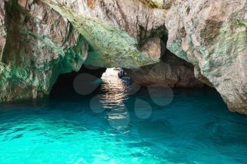 Coastal rocks of Capri island, small empty grotto with shining sea water inside