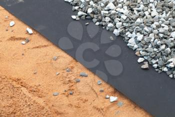 Geotextile layer between gray gravel and sandy ground