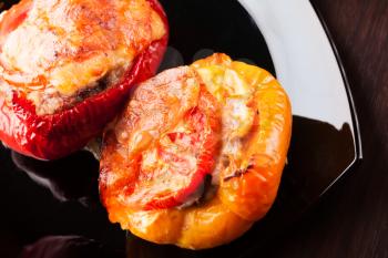 Stuffed bell peppers with chopped meat, cheese and tomato on black plate