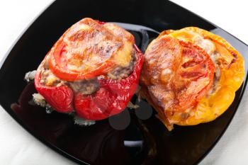Two stuffed bell peppers with chopped meat, cheese and tomato on black plate