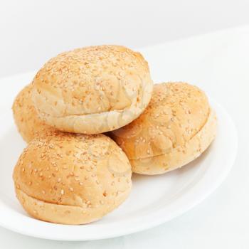Four small buns for hamburgers lay on white plate