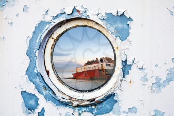 Ship wreck behind round porthole in white and blue wall 