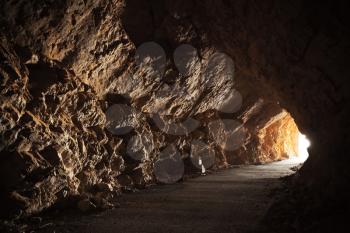 Empty road goes through the cave with glowing end