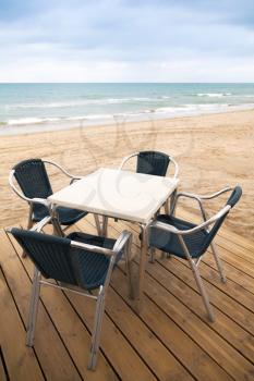 Open space sea side bar interior with wooden floor and metal armchairs on sandy beach