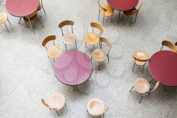 Round tables and chairs around stand in an empty cafe interior, top view