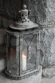 Old metal lamp with burning candle stands on stone stairs