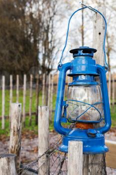 Blue vintage kerosene lamp hangs on wooden outdoor fence