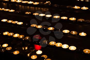Small candles in rows burning on shelves in dark catholic church