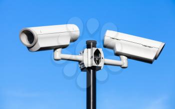 Two closed-circuit television cameras mounted on black pole above blue sky
