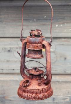 Old rusted red kerosene lamp on gray wooden wall background