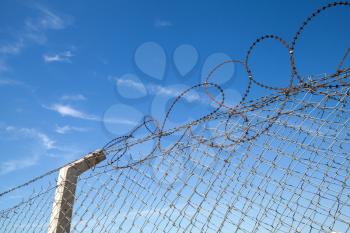 Metal fence with barbed wire over blue sky background