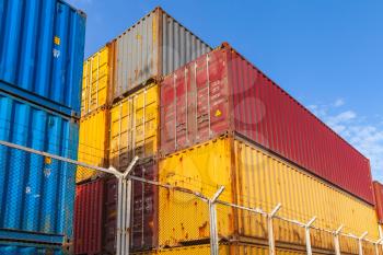 Colorful Industrial cargo containers are stacked behind metal fence with barbed wire