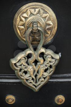 Old copper door knob with Arabic pattern on black wooden gate. Izmir, Turkey