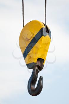 Crane hook hanging on steel ropes over cloudy sky background