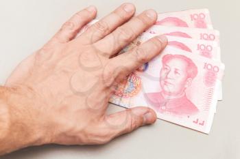 Chinese 100 yuan renminbi banknotes and male hand over white office table surface