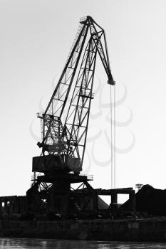 Dark silhouette of industrial port crane. Bulgaria, Danube River coast. Black and white vertical photo