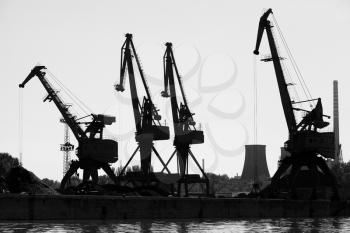Dark silhouettes of industrial port cranes. Danube River, Bulgaria. Monochrome photo