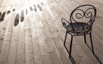 Old black wrought-iron chair standing on wooden floor, outdoor photo