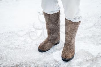 Male feet with traditional Russian felt boots on winter road with snow and ice 