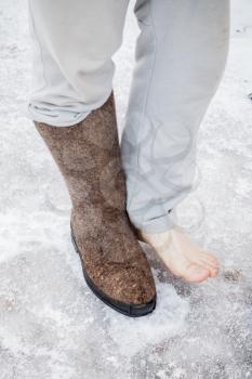 Male feet with one traditional Russian gray felt boot stand on icy road