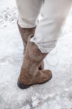 Male feet with traditional Russian felt boots stand on winter road with snow and ice 