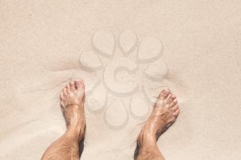 Wet male feet stand on white coastal sand
