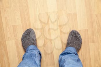 Male feet in blue pants and gray woolen socks stand on wooden parquet