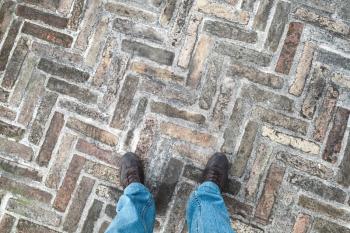 Feet of an urbanite man in jeans standing on old cobblestone pavement