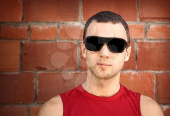 Closeup portrait of young man in black sunglasses over old brick wall