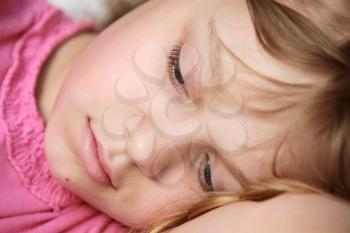 Closeup portrait of lying little blond Caucasian girl in pink