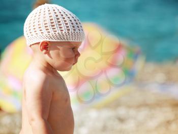 Outdoor summer profile portrait of Caucasian baby girl in white hat on the beach