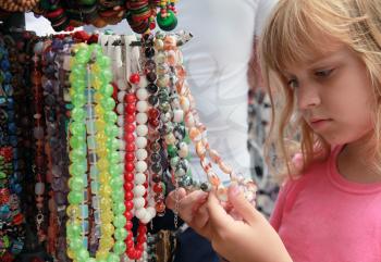 Little blond girl in the souvenir market considers colorful stone beads