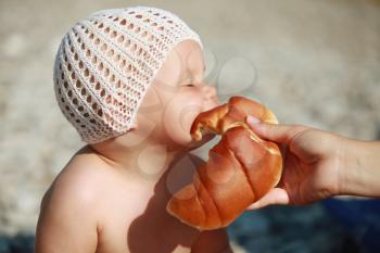 Little Caucasian baby eats with pleasure croissant on the beach